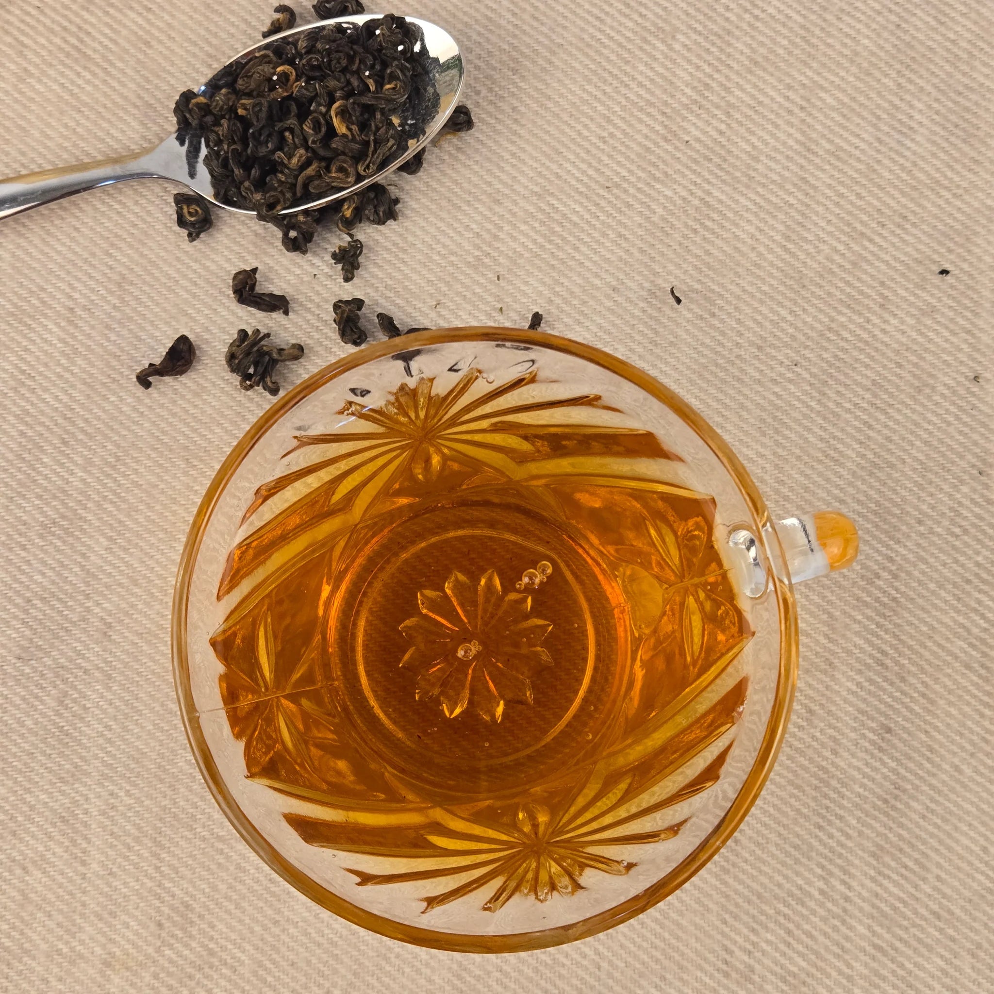 Tea cup with floral design, spoonful of tea leaves, and loose tea leaves on a beige background