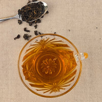 Tea cup with floral design, spoonful of tea leaves, and loose tea leaves on a beige background
