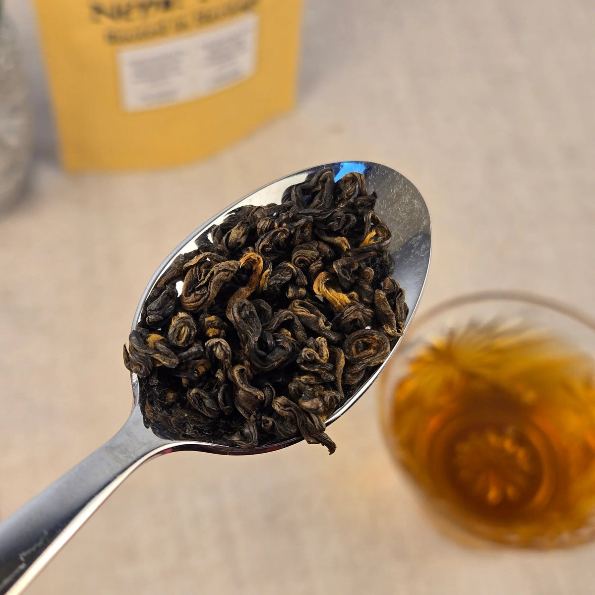 Spoonful of dar oolong tea leaves with a blurred glass of tea in the background