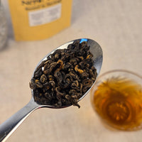 Spoonful of dar oolong tea leaves with a blurred glass of tea in the background