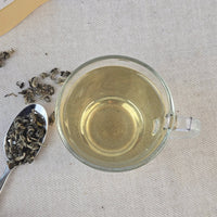 Clear glass mug with green tea and tea leaves on a light fabric background