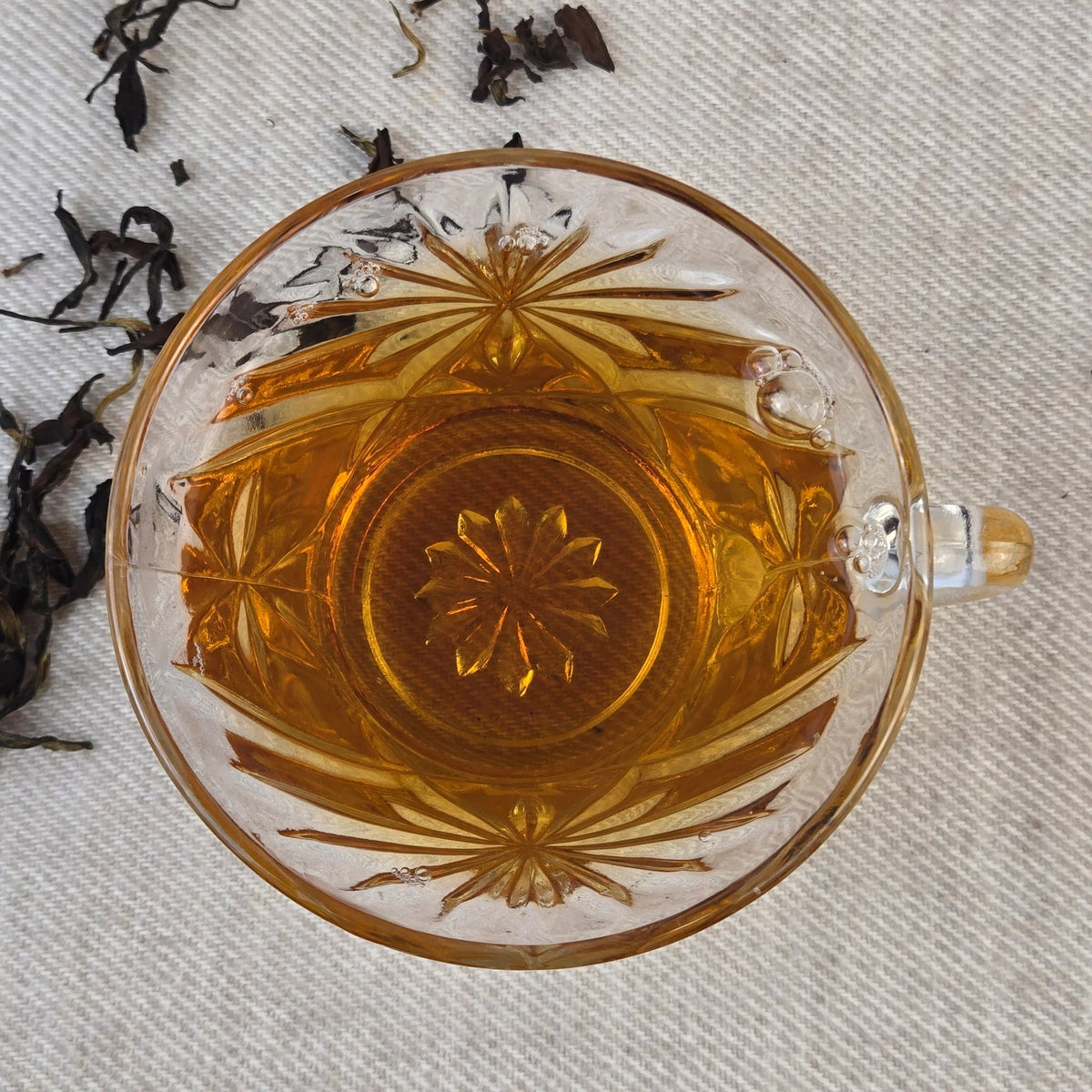 Decorative glass with amber liquid of floral oolong tea on a textured fabric background