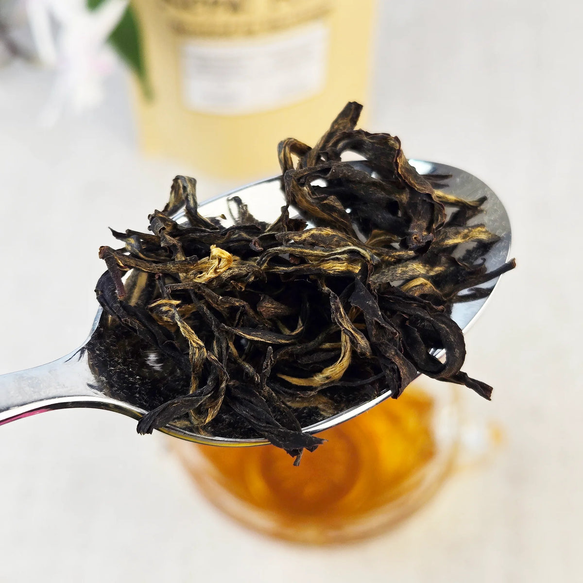 Floral oolong Tea leaves on a spoon with a blurred tea container in the background