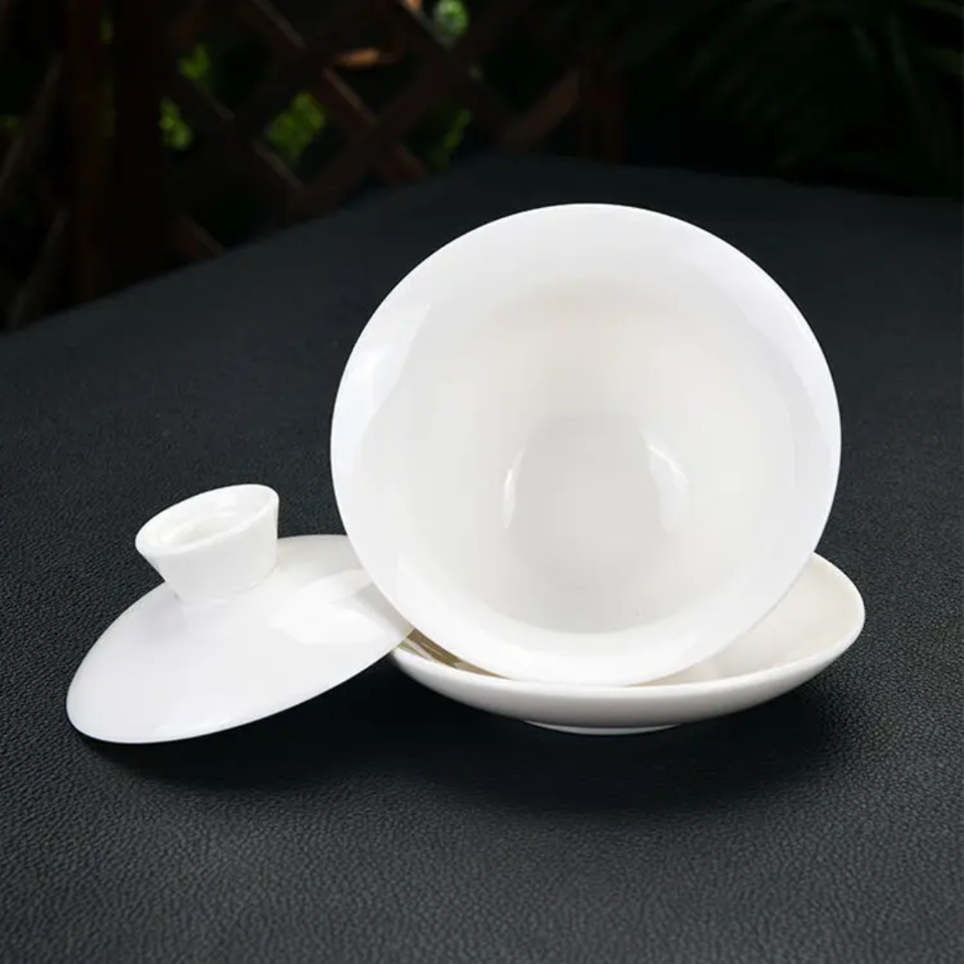 Hand pouring tea from a white gaiwan into a cup