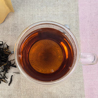 Clear glass mug filled with muscatel black tea liquid on a textured surface.