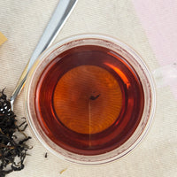 Tea cup with red liquid and tea leaves on a textured surface